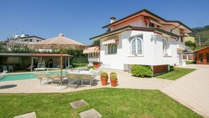 En hvid villa med swimmingpool, udendørs møbler og krukker med planter.