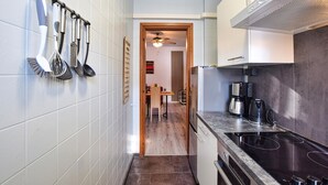 Une cuisine étroite aux murs recouverts de carreaux blancs, une porte en bois donnant sur un coin repas, et une cuisinière moderne.