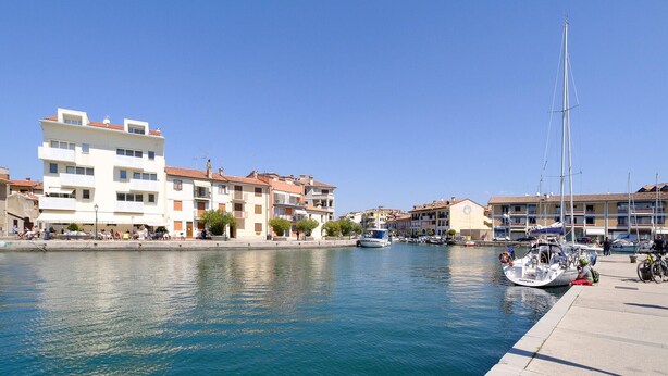 Un port de plaisance avec des bateaux amarrés, une promenade en bord de mer et des immeubles à plusieurs étages dotés de balcons.