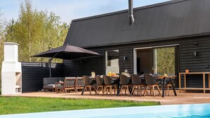 A modern outdoor dining area with a pool, wooden furniture, and a large umbrella. - Lovely home in Væggerløse with sauna (Væggerløse)