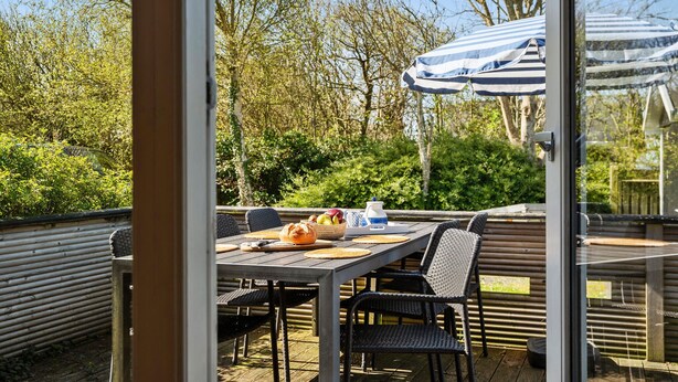 An outdoor dining area with a table set for two, surrounded by wicker chairs, a striped umbrella, and a basket of fruit. - Nice home in Esbjerg V with WiFi (Esbjerg V)