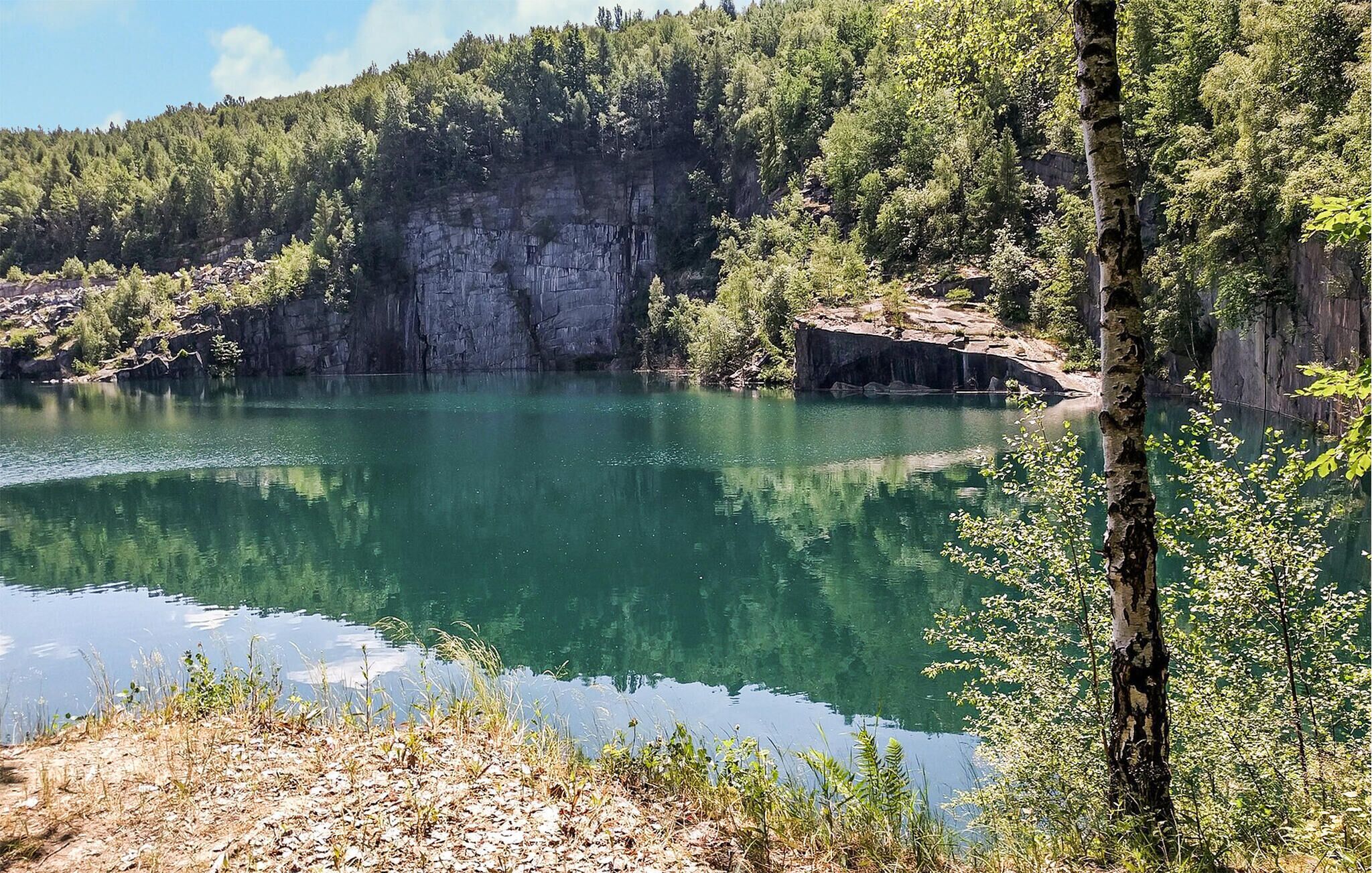 A natural landscape with a clear lake surrounded by dense forest and rocky cliffs.