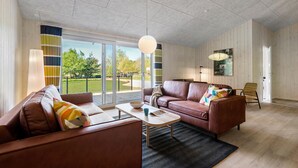 A spacious living room with leather sofas, a coffee table, and a large window offering a view of a park. - Awesome home in Oksbøl with sauna (Oksbøl)