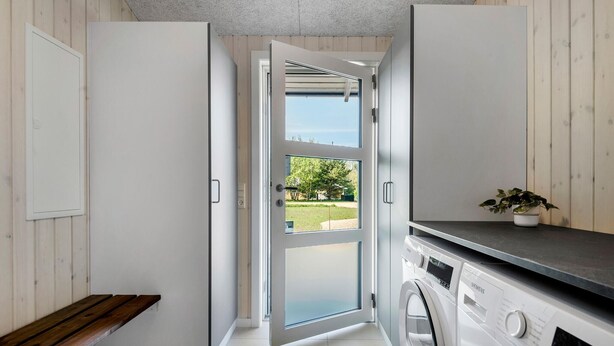 A laundry area with a washing machine, a bench, and a view of the outdoors through a glass door. - Awesome home in Oksbøl with sauna (Oksbøl)
