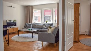 En moderne stue med en grå sofa, et fjernsyn og et træskab.