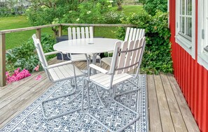 Une table ronde entourée de quatre chaises, posée sur une terrasse en bois, le tout agrémenté d’un tapis à motifs.