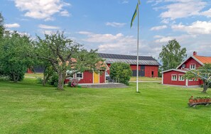 Une grange rouge avec une porte jaune, entourée d’herbe verte et d’arbres.