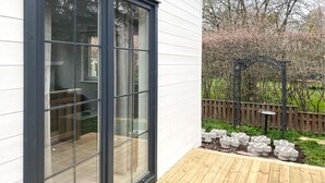 A wooden deck with a glass door leading to a garden area with a wooden fence and a bird bath.
