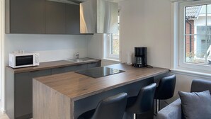 A modern kitchen with a central island, bar stools, a microwave, and a coffee maker.