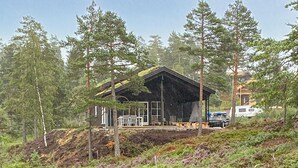 A cabin with a sloped roof, surrounded by tall pine trees, and a small deck area with outdoor furniture. - Stunning home in åmli with house a mountain view (Åmli)