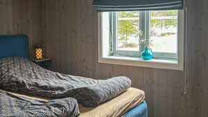 A bedroom with a bed, a nightstand, a window with a view of trees, and a vase with flowers on the windowsill. - Stunning home in åmli with house a mountain view (Åmli)