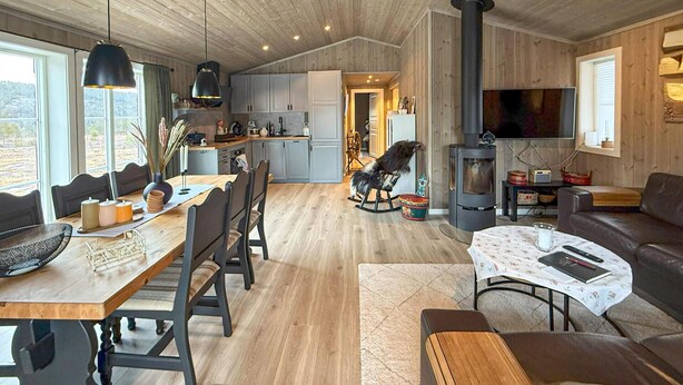A spacious living room with a wooden floor, a dining area with a long table and chairs, a kitchen with modern appliances, and a large TV mounted on the wall. - Stunning home in åmli with house a mountain view (Åmli)