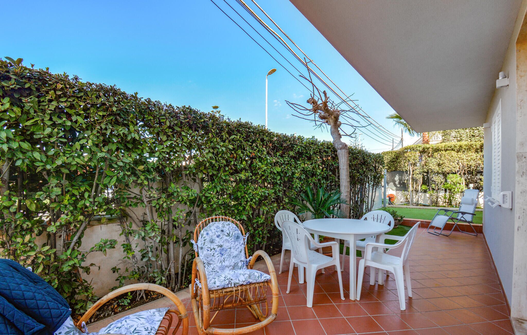 Een terras met een tafel en stoelen, omringd door groen en een betegelde vloer.