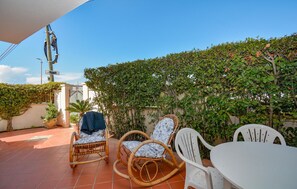 A patio with wicker chairs and a table, surrounded by a hedge and a building. - Awesome apartment in Marina di Modica (Marina di Modica)