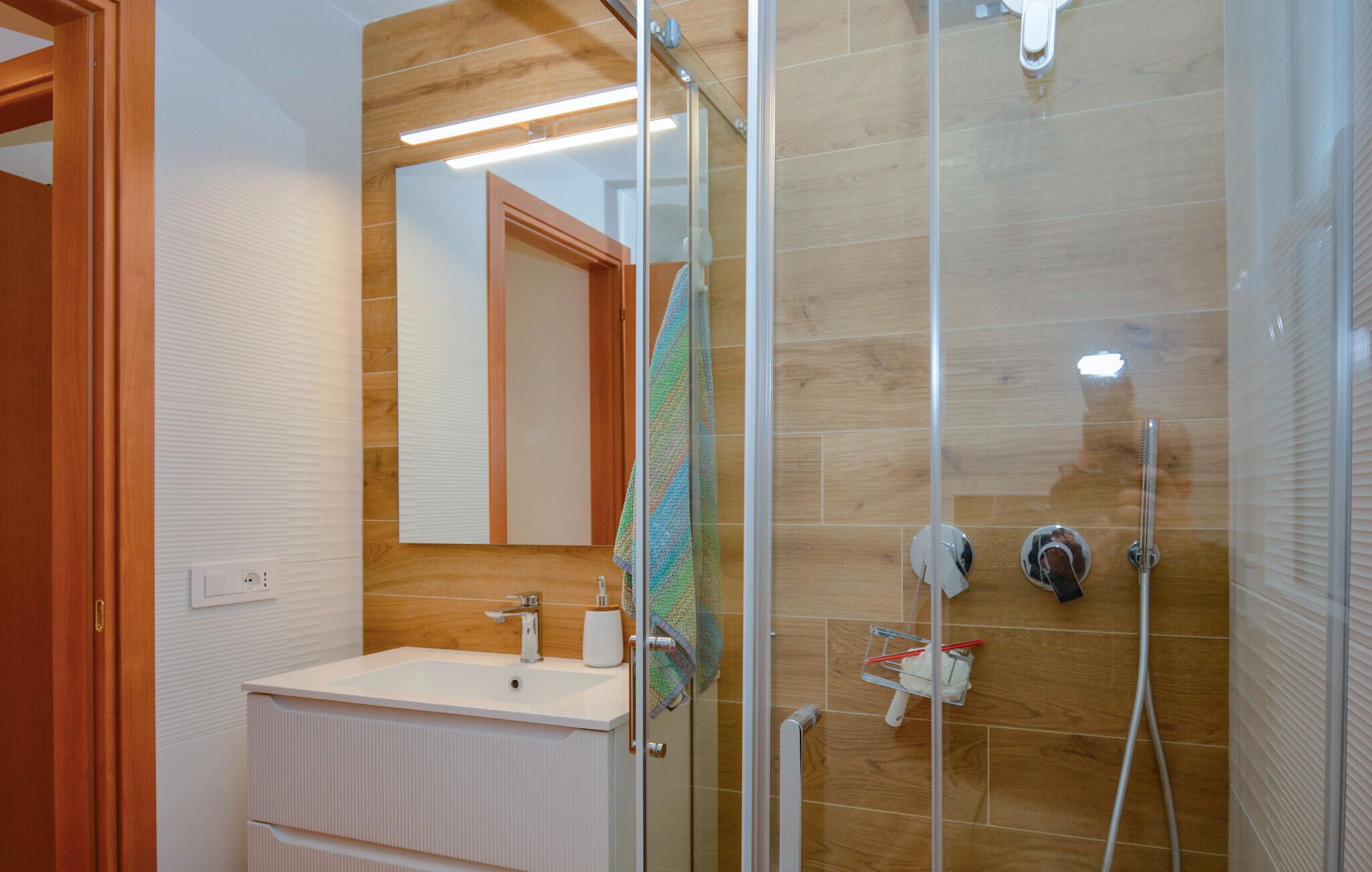 A modern bathroom with a glass shower enclosure, a sink with a mirror, and a towel hanging on the wall.