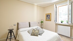 A bedroom with a bed, a small stool, a radiator, a window with plants, and a framed picture on the wall. - Pet friendly apartment (Soiano del Lago)
