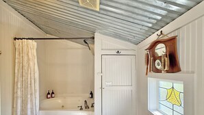 A bathroom with a bathtub, a shower curtain, a private door, a mirror with a clock, and a window with a stained glass design.