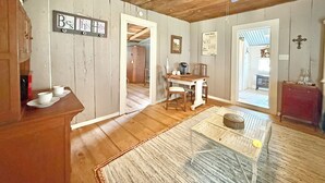 A rustic interior with wooden floors, a dining area with a table and chairs, a ceiling fan, and a sign on the wall.