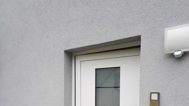 Ein modernes Äußeres mit einer weißen Tür, einem Metallgeländer und einer strukturierten Wand.