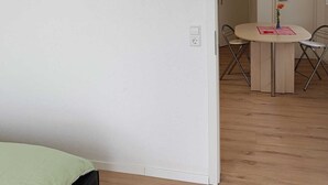 Ein Zimmer mit einem Bett, einem Esstisch mit Stühlen und einer Tür zu einem anderen Raum.