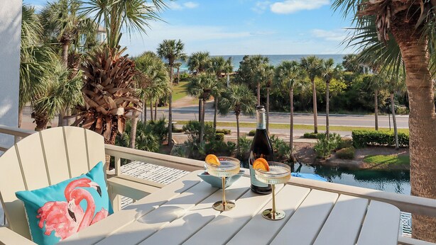 A balcony with a view of a pool and palm trees, a bottle of champagne, and a cocktail glass with an orange slice.