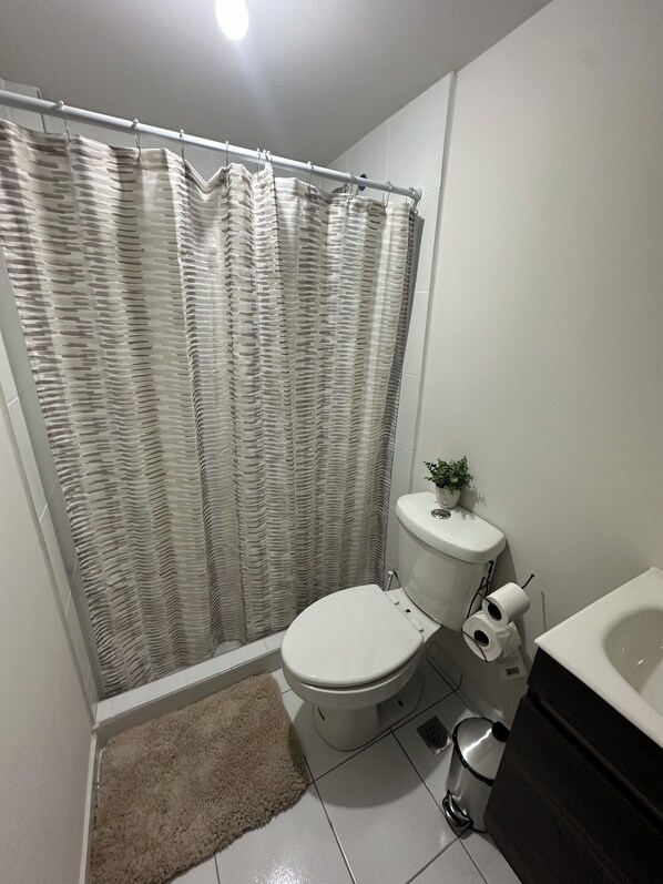 Un bagno con tenda della doccia, water, bidet e una piccola pianta sul serbatoio del water.