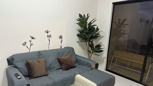 Ein Ecksofa mit Fernbedienung, einem Blumentopf und einer Glastür, die auf einen Balkon führt.