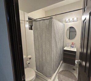 Un bagno con tenda da doccia, toilette, lavandino e uno specchio illuminato.