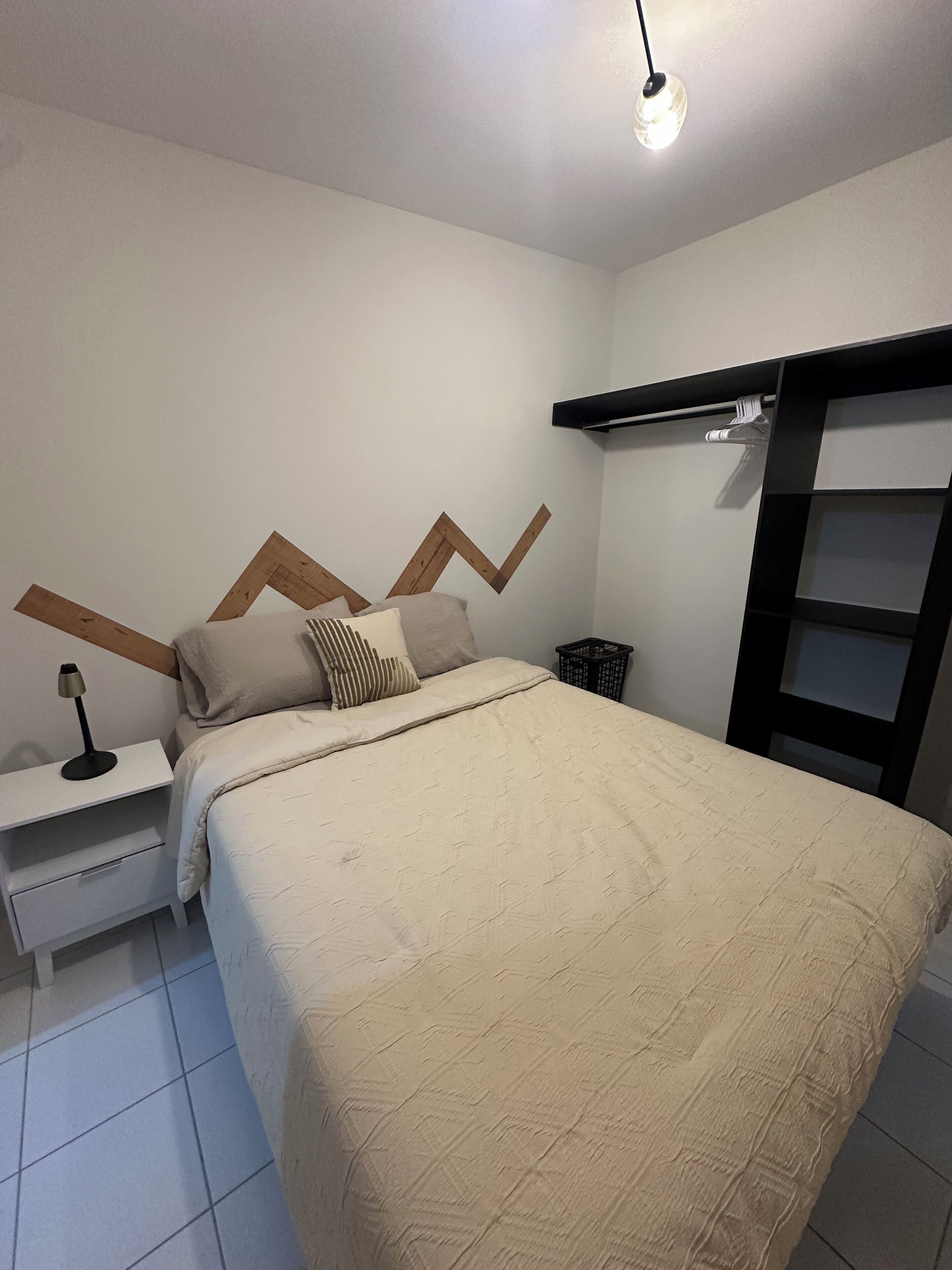 Ett sovrum med en säng, två sängbord, en lampa, en byrå och en hylla som är monterad på väggen.