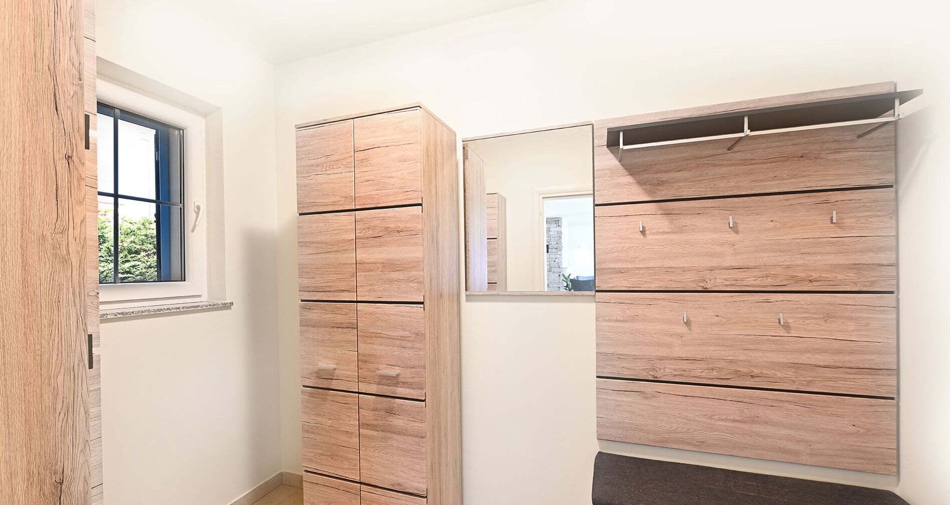 Un couloir avec une armoire en bois, un miroir et une fenêtre.