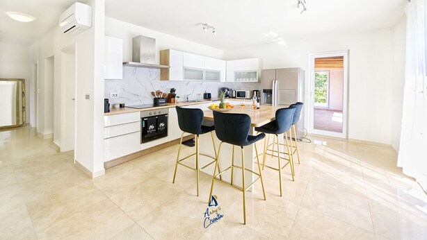 Een moderne keuken met witte kasten, een centraal eiland met barstoelen en uitzicht naar buiten.