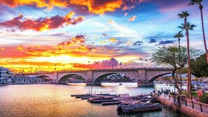 Ein Fluss mit einer Brücke, Booten und Palmen bei Sonnenuntergang.
