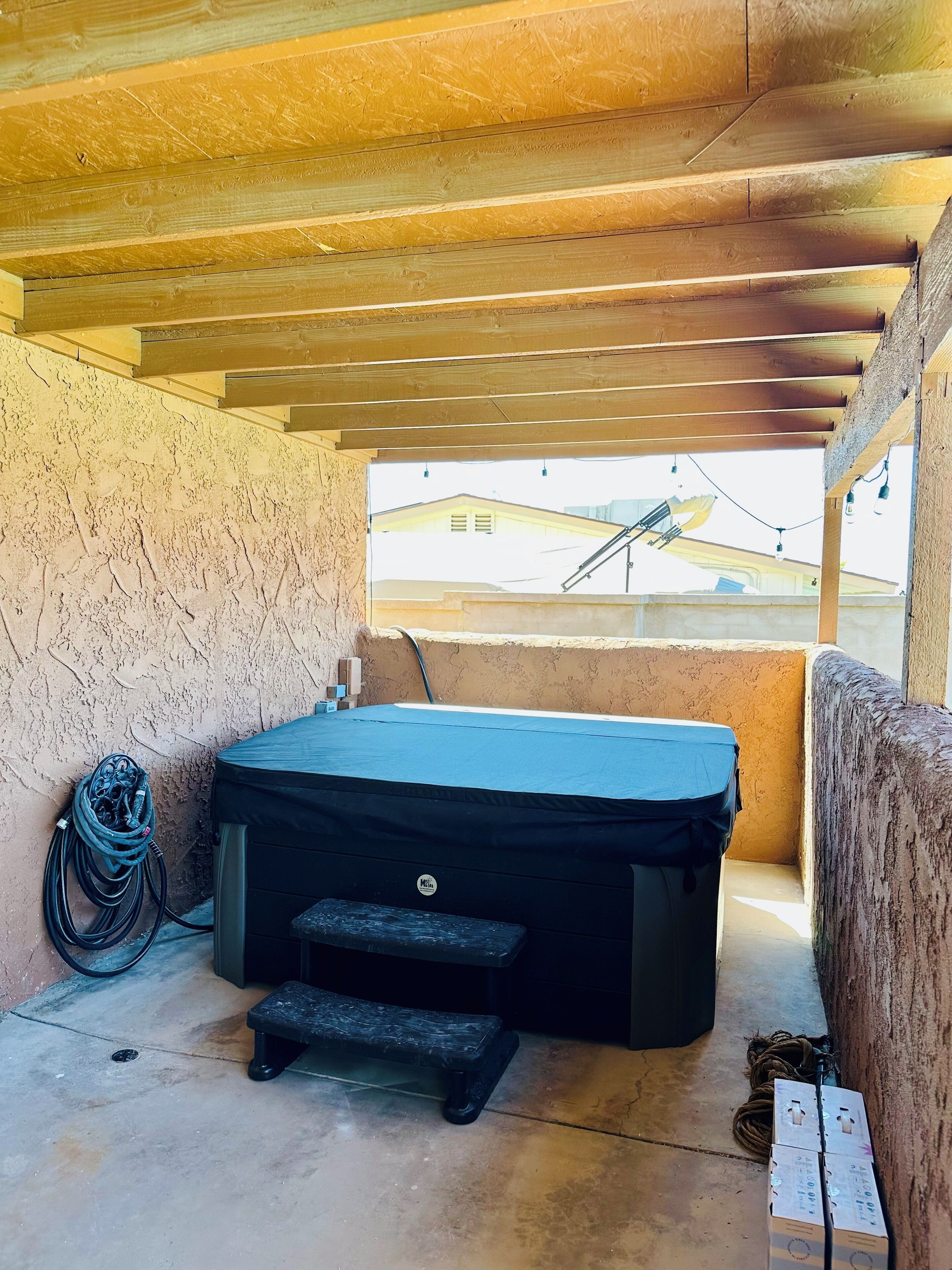 A covered outdoor area with a hot tub, a hose, and a step leading to it.