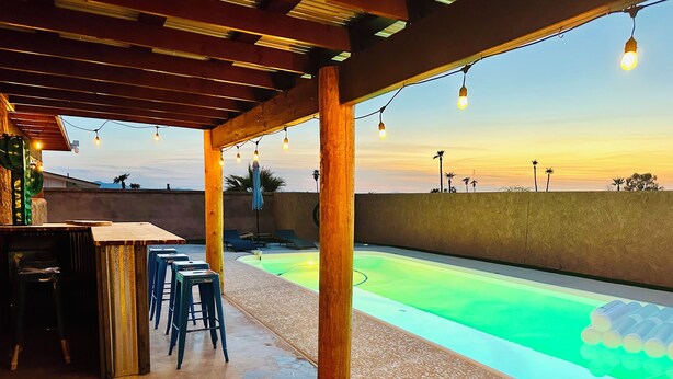 Ein Außenpoolbereich mit einer Holzpergola, Liegestühlen und einer Bar.
