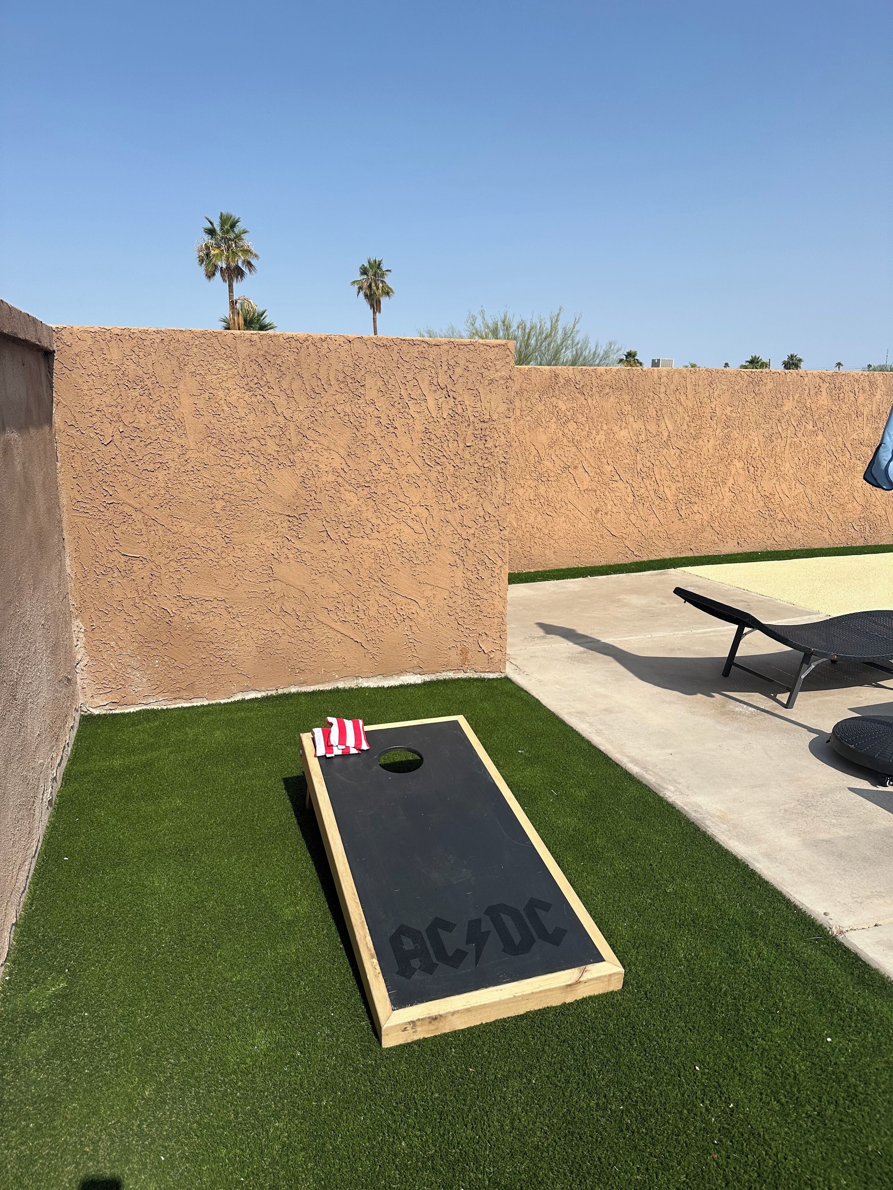 Un jardin avec un jeu d’extérieur en bois aux couleurs d’AC/DC, de l’herbe artificielle, une terrasse en béton et un mur en pierre.