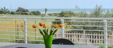 A table with a green vase of tulips on a balcony overlooking a coastal view.