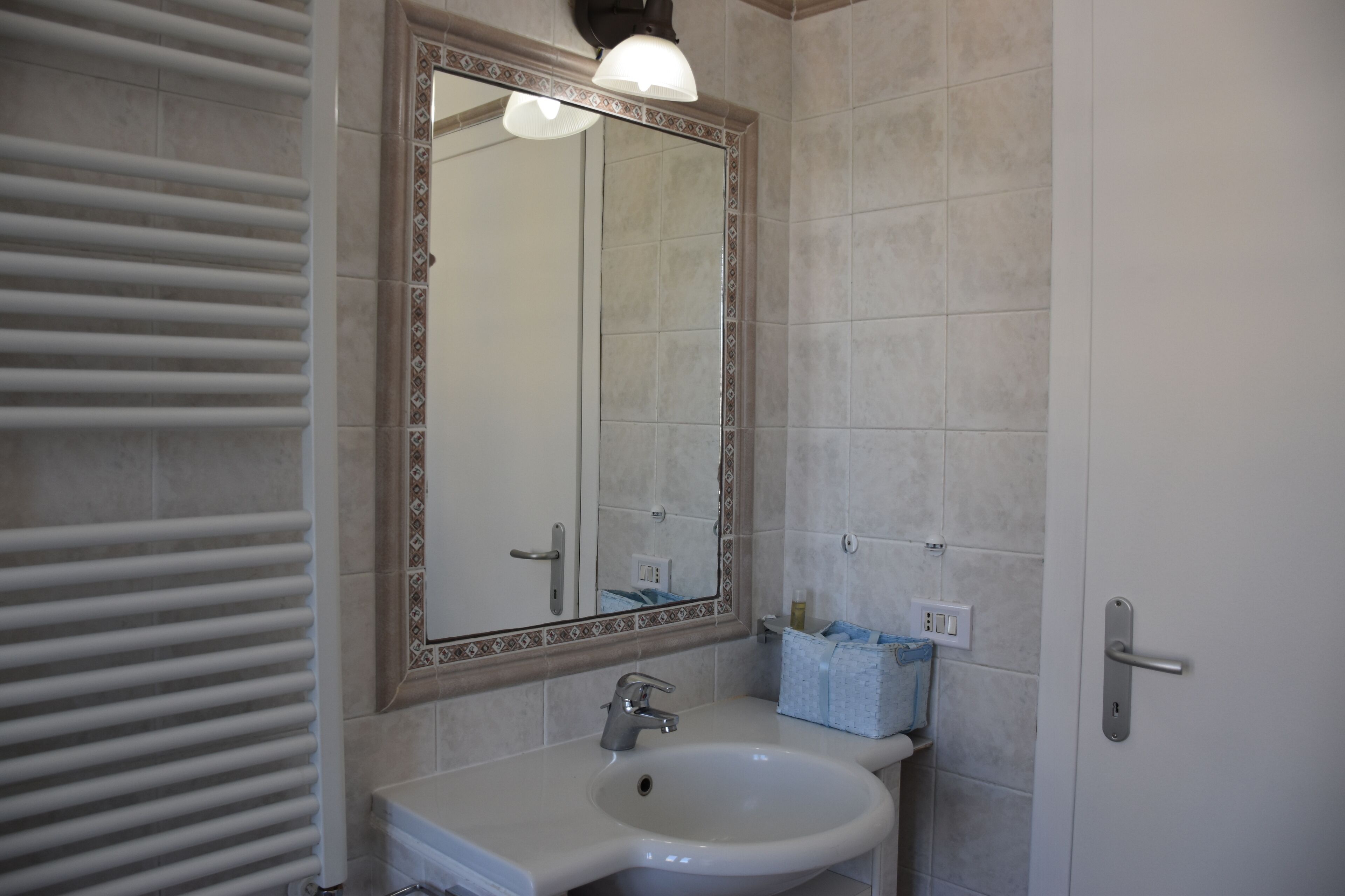 A bathroom with a white sink, a mirror with a decorative frame, a towel rack, and a door with a handle.