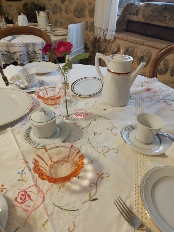 Una mesa de comedor dispuesta con platos, tazones y una tetera blancos. Hay un florero con una flor roja sobre la mesa.
