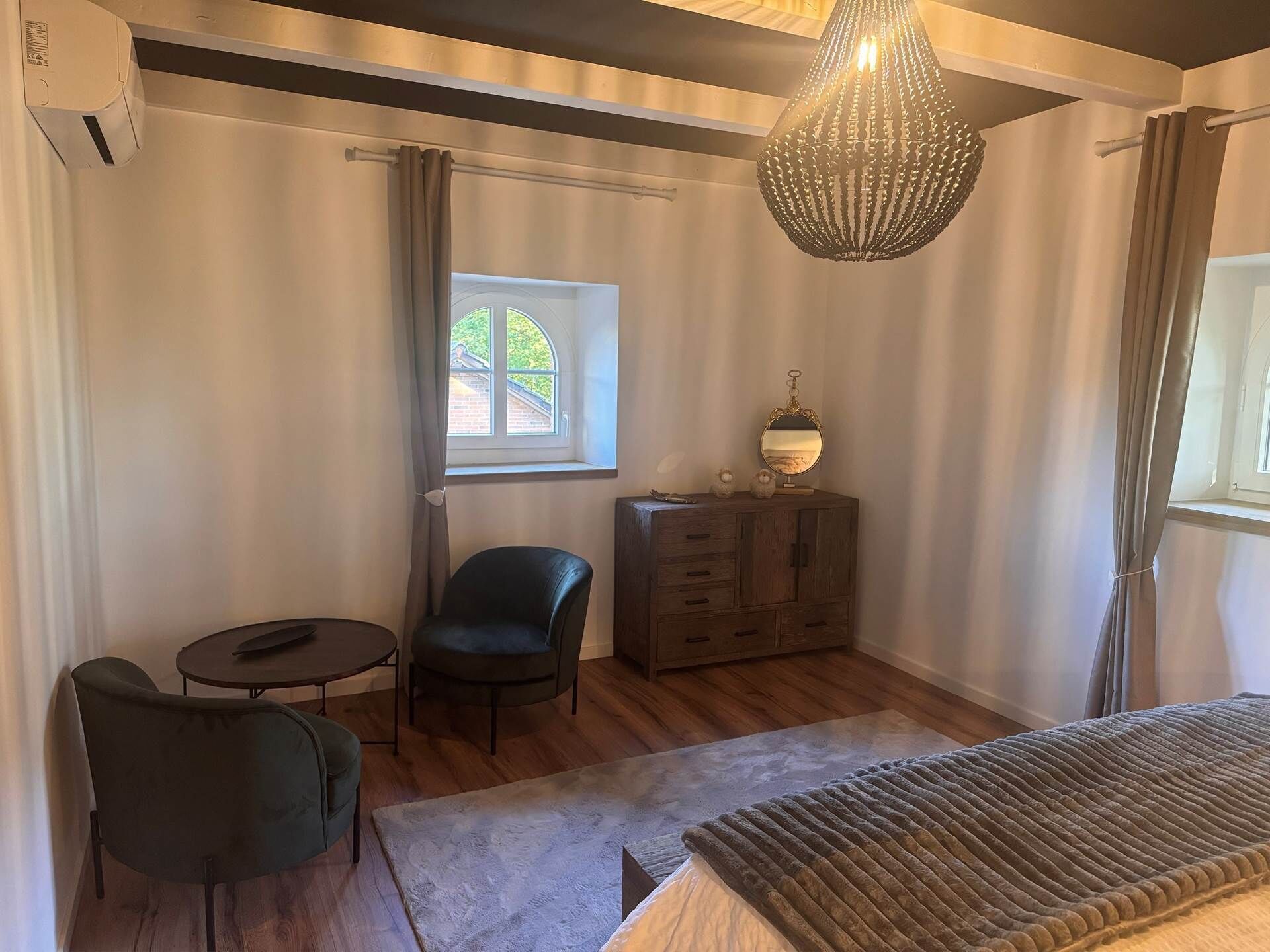 A room with a bed, a dresser, a chair, a small table, and a window with curtains.