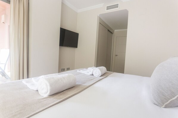 Een hotelkamer met een opgemaakt bed, een flatscreen televisie aan de muur en een deur naar een andere kamer.