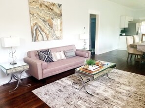A modern living room with a pink sofa, a glass coffee table, and a large abstract painting on the wall. - Relax at This RVA Cape Cod Gem! (Richmond)