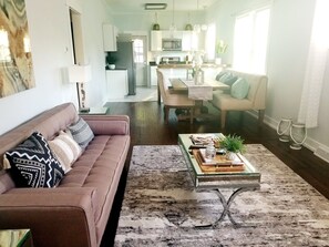 A modern living room with a sofa, coffee table, and a view into the kitchen. - Relax at This RVA Cape Cod Gem! (Richmond)