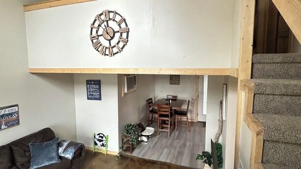 A spacious living area with a high ceiling, a wooden staircase, a dining table with chairs, and a couch with cushions.