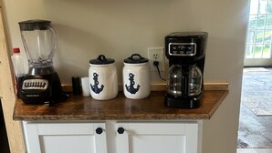 A kitchen counter with a blender, two canisters, and a coffee maker. - Charming lake cottage overlooking Grand lake (Grove)