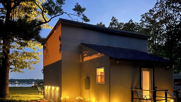 A small, single-story building with a sloped roof, a porch with a railing, and a small window. - Charming lake cottage overlooking Grand lake (Grove)