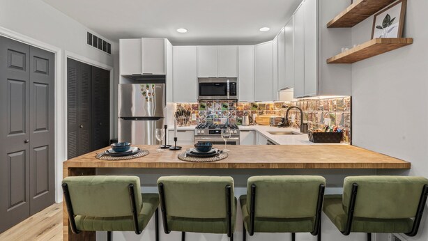 Una cocina moderna con una isla central, armarios blancos y taburetes de bar verdes.