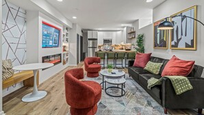 Una sala de estar moderna con un sofá negro, sillones rojos, una mesa de centro blanca y una cocina al fondo.