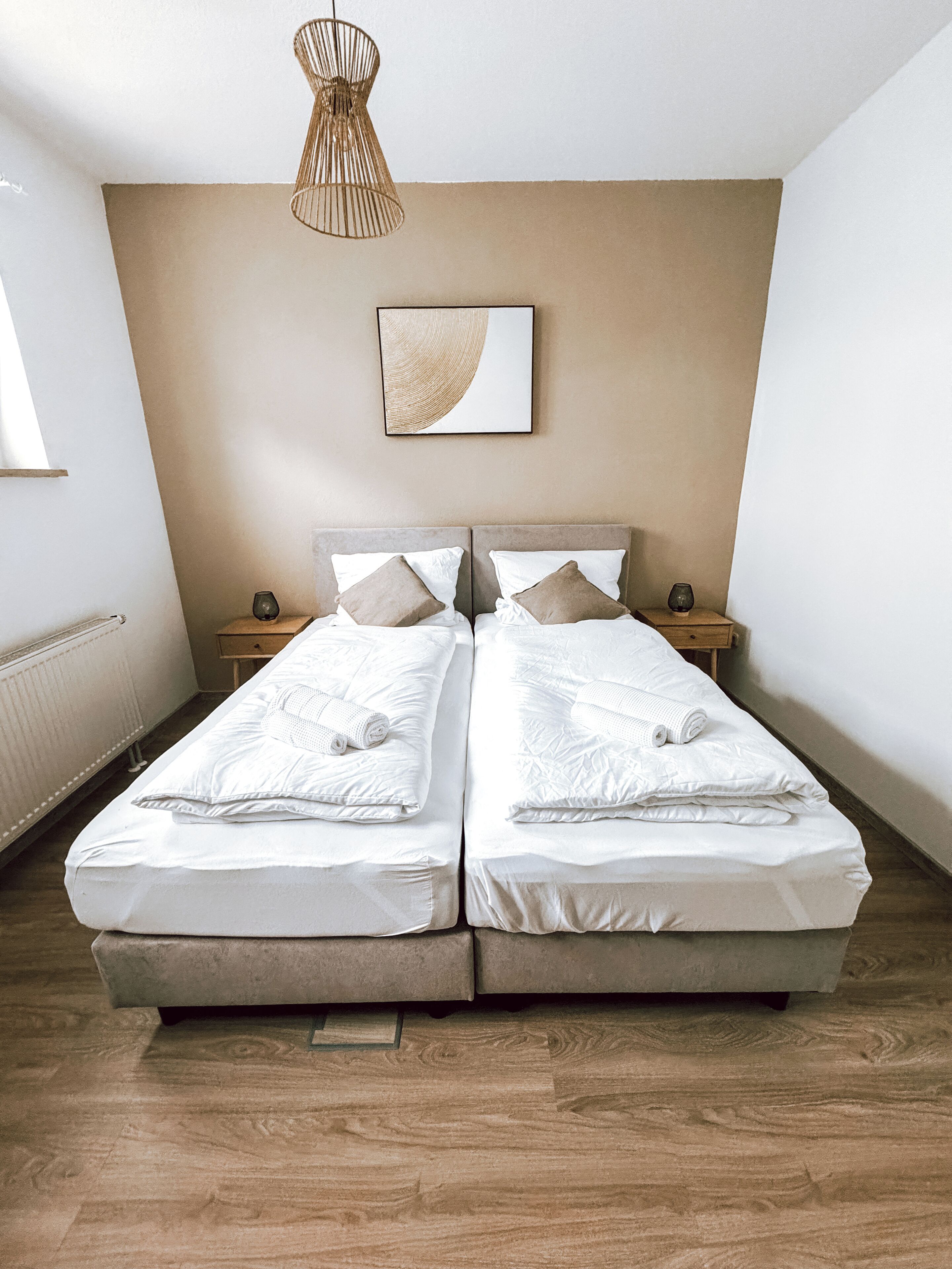 Un lit double avec du linge de lit blanc et deux oreillers, une table de chevet avec une lampe et une œuvre d’art accrochée au mur.