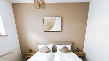 Un lit double avec du linge de lit blanc et deux oreillers, une table de chevet avec une lampe et une œuvre d’art accrochée au mur.