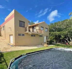 A two-story building with a balcony, a swimming pool, and a grassy yard.